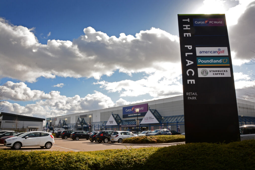 Entrance sign for The Place Retail Park listing Currys PC World, American Golf, Poundland and Starbucks