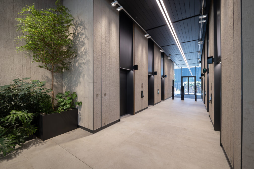 Lift lobby at Osmo Nine Elms, with stone-clad walls, planting and a glazed entrance beyond